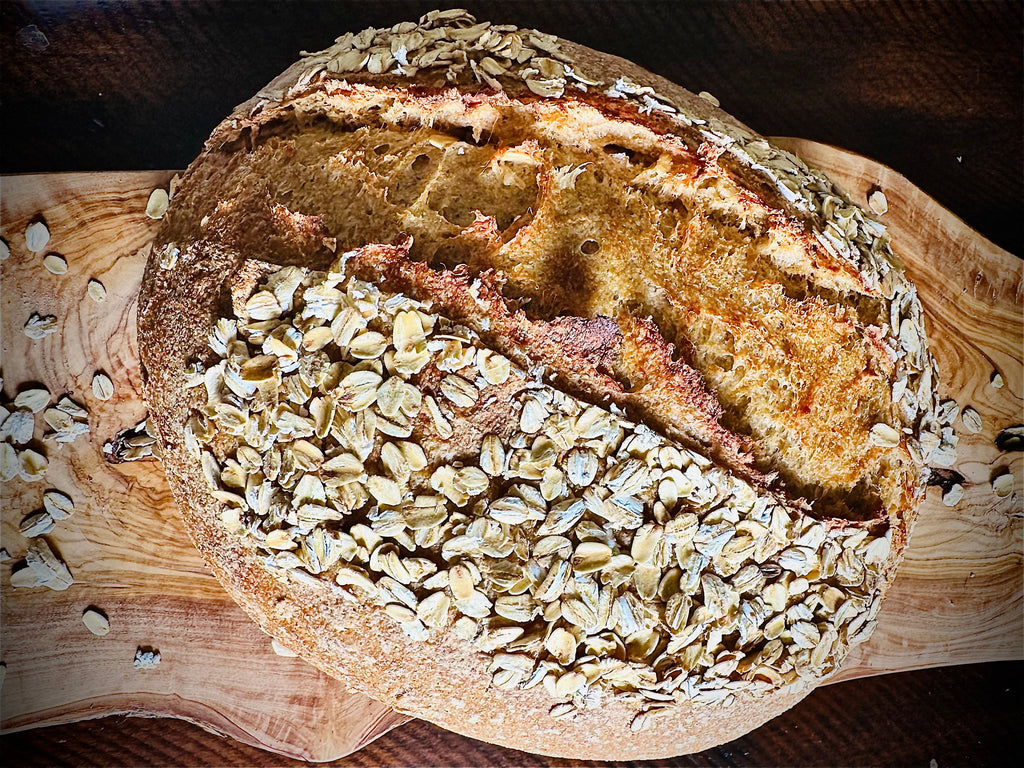 Fresh-milled artisan sourdough bread loaf with oats on a wooden cutting board by Silo and Stone Co Dallas